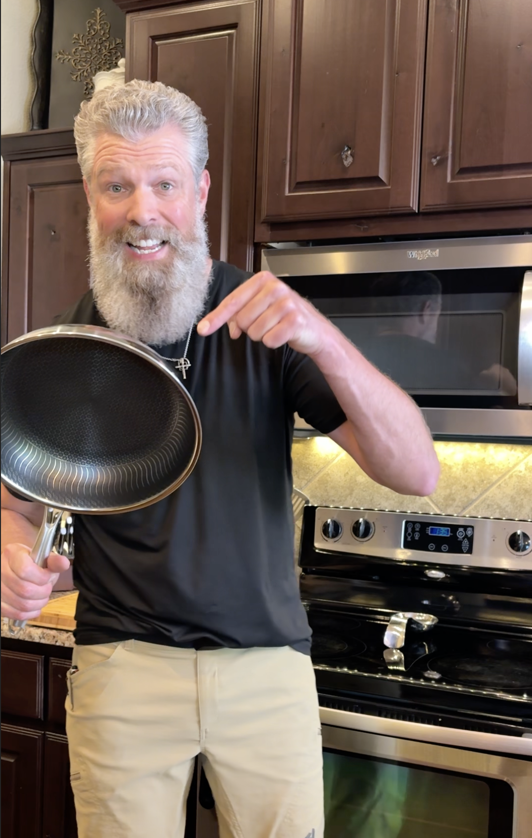 Man with a beard holding a frying pan in a kitchen.