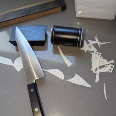 Knife, cut paper strips, and a cylindrical container on a table.