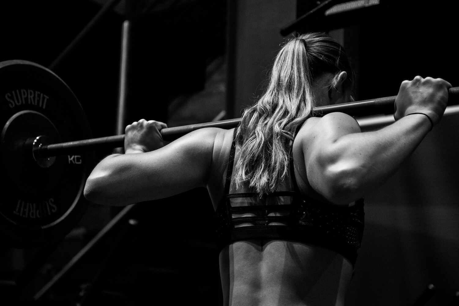 Person lifting a barbell, seen from behind in black and white.