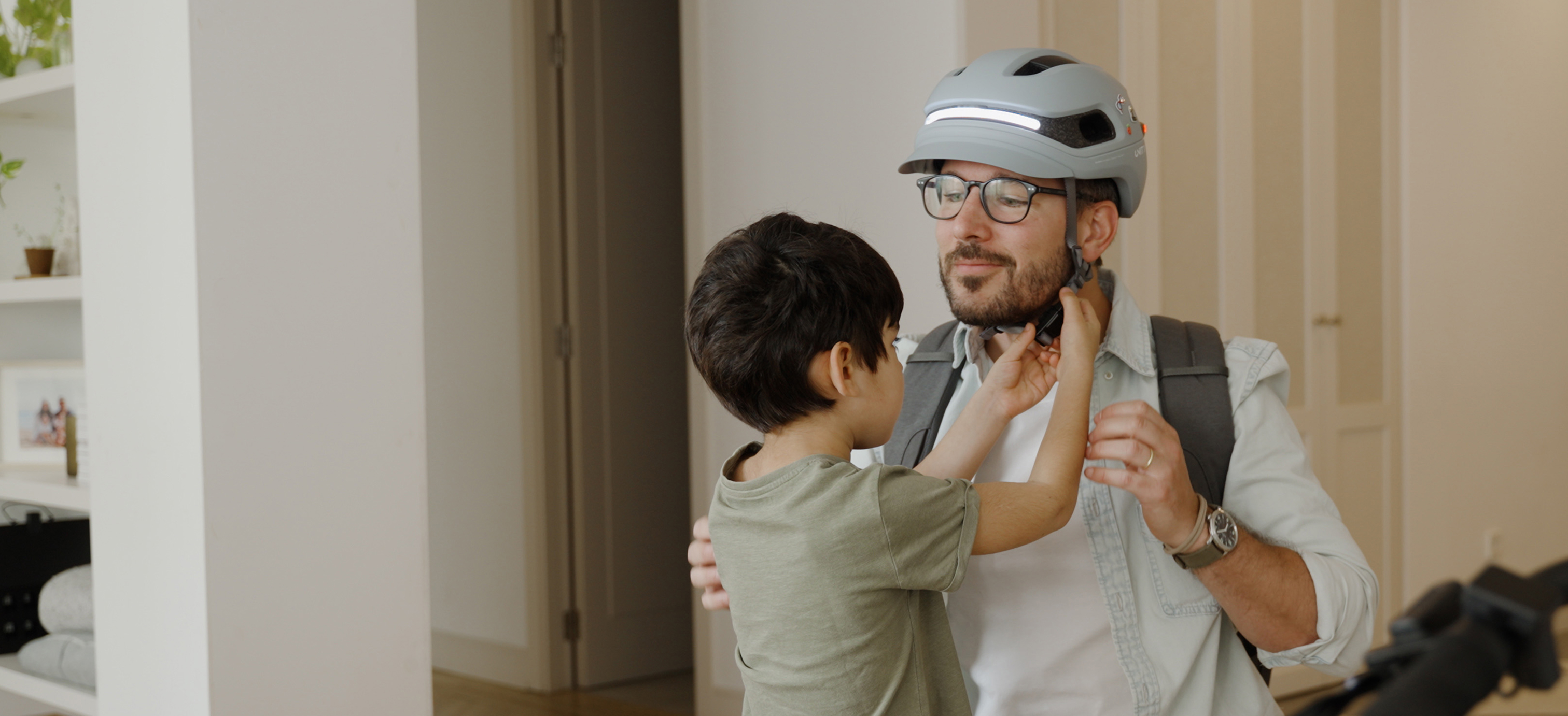 Child helping an adult adjust a bicycle helmet indoors.