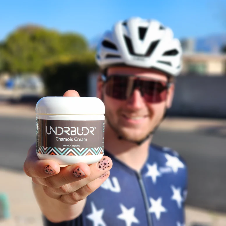 Person holding a container of chamois cream, wearing cycling gear and helmet.
