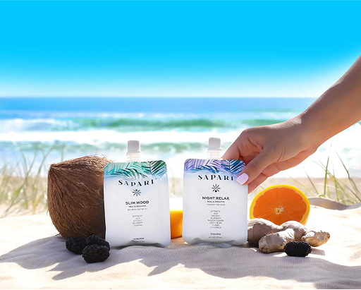 Hand holding two pouches on a beach with coconut, orange, and ginger.