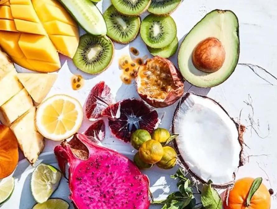 Assorted fresh fruits including avocado, kiwi, mango, and coconut on a white background.