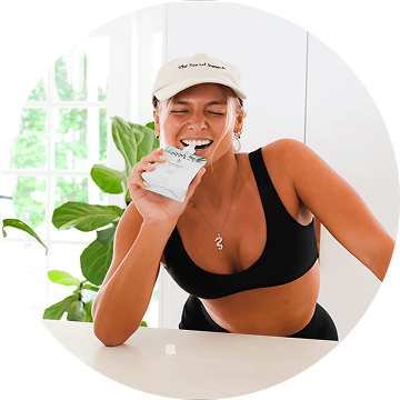 Person in a black top drinking from a carton, standing by a plant.