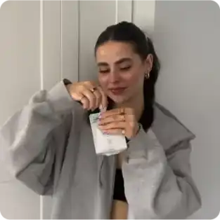 A person in a gray jacket is holding and opening a small container.