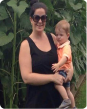 Woman holding a child, standing in front of large green plants.