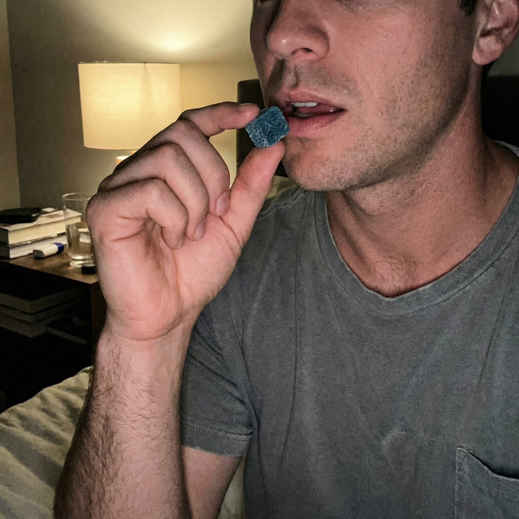 A close-up of a man in a grey t-shirt holding a blue gummy candy to his mouth.