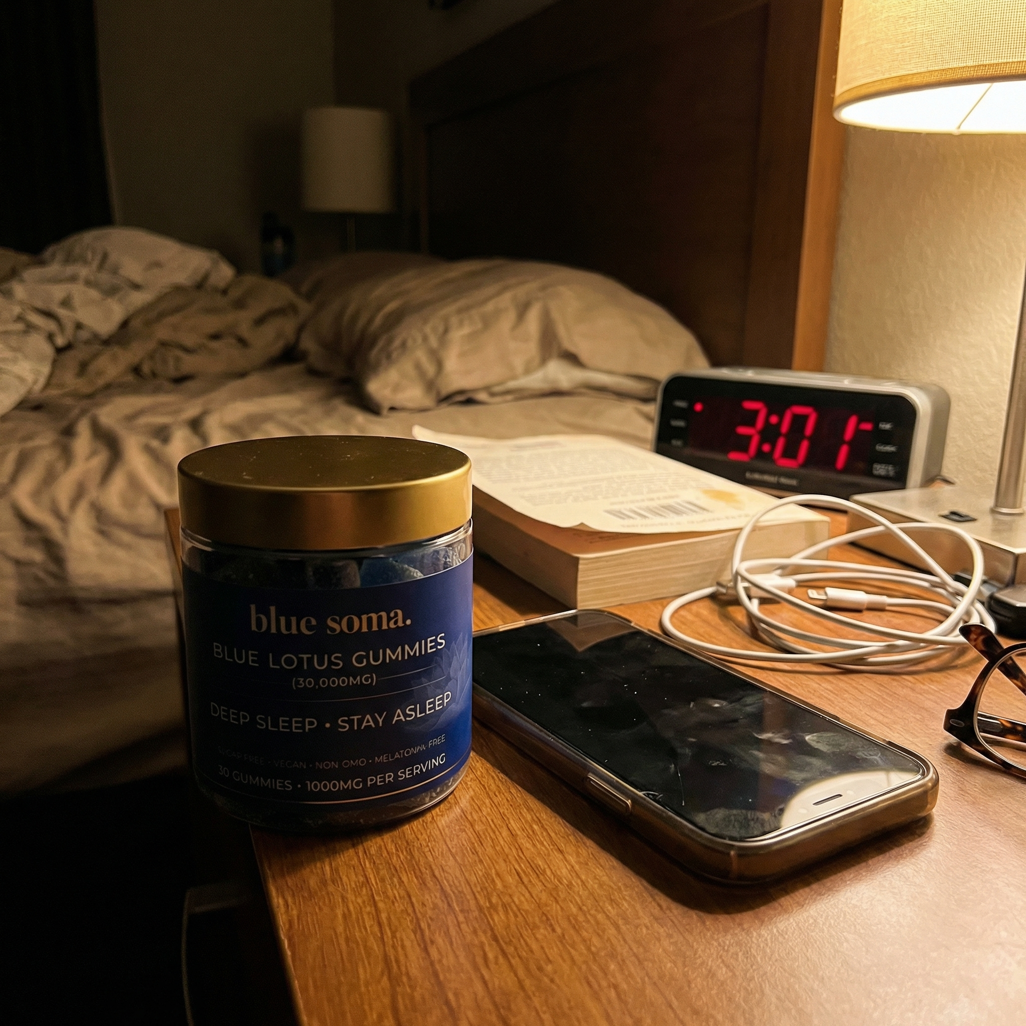 A jar of Blue Lotus Gummies on a bedside table next to a phone and a digital clock showing 3:01.