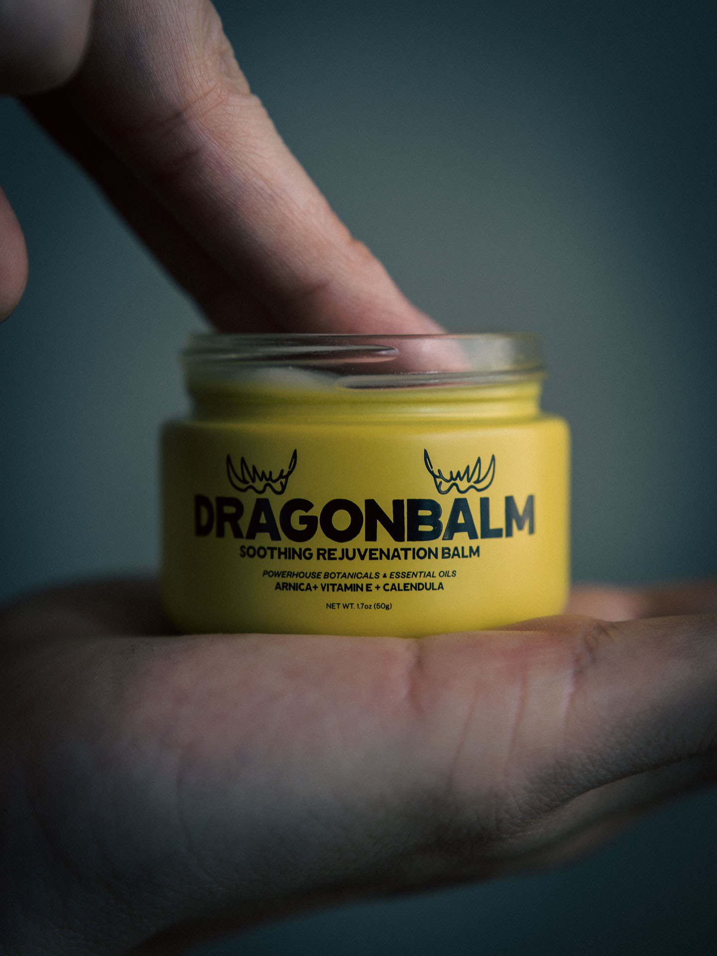 Hand holding a jar of Dragon Balm with a finger dipping inside.