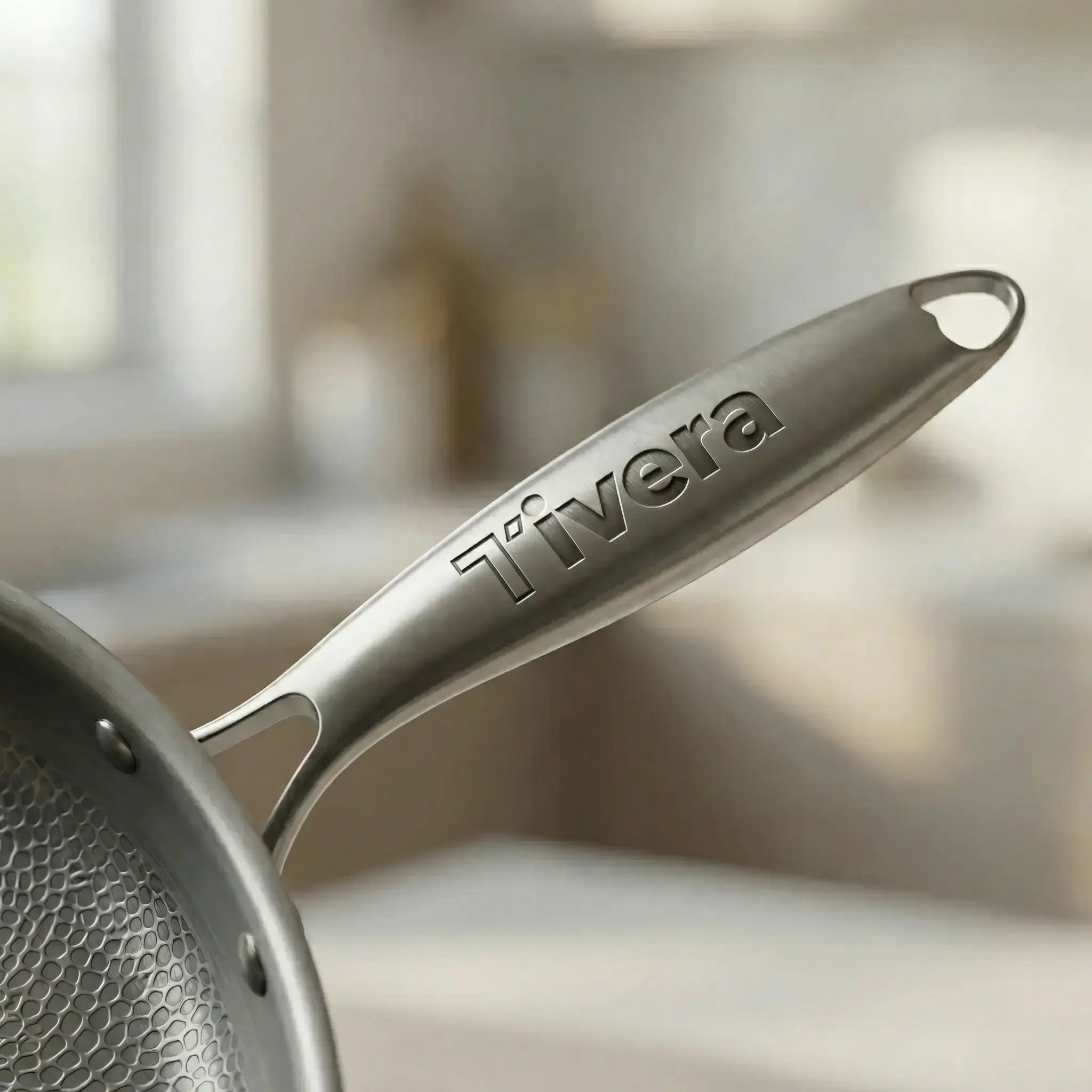 A close-up of a stainless steel pan handle with the brand name 'Tivera' engraved on it.