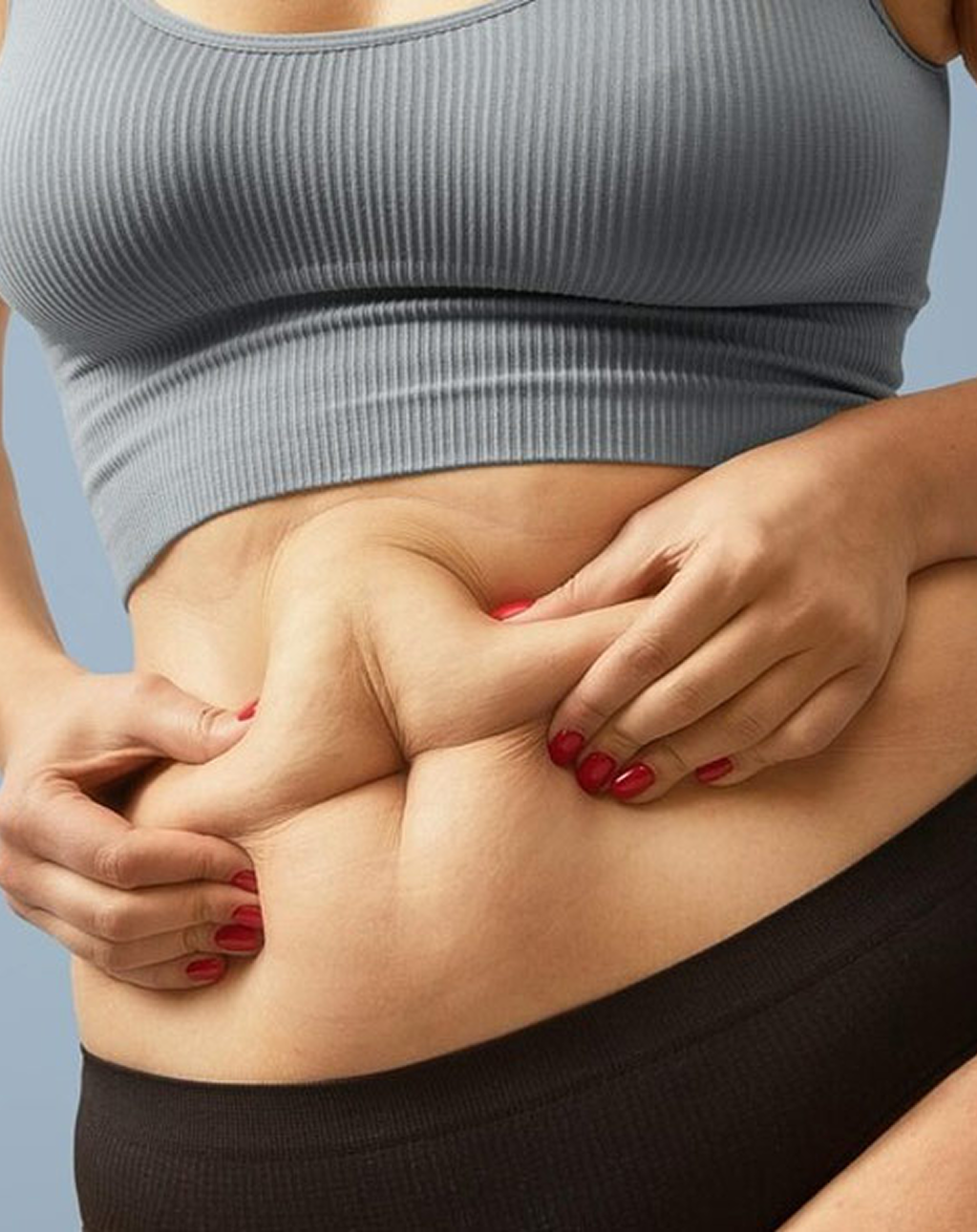Person pinching their stomach skin, wearing a gray top and black bottoms.