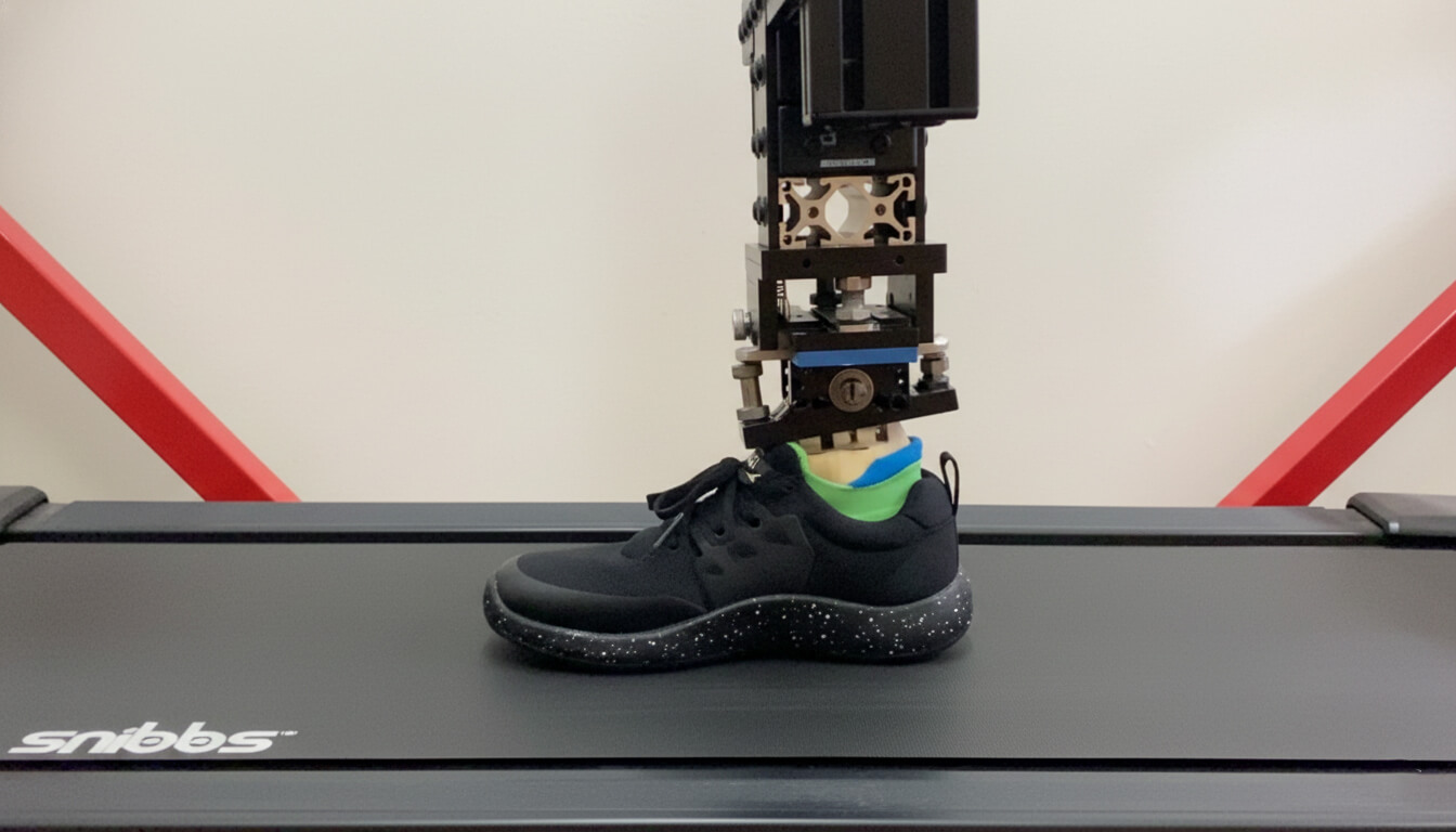 Robotic leg wearing a black sneaker on a treadmill.