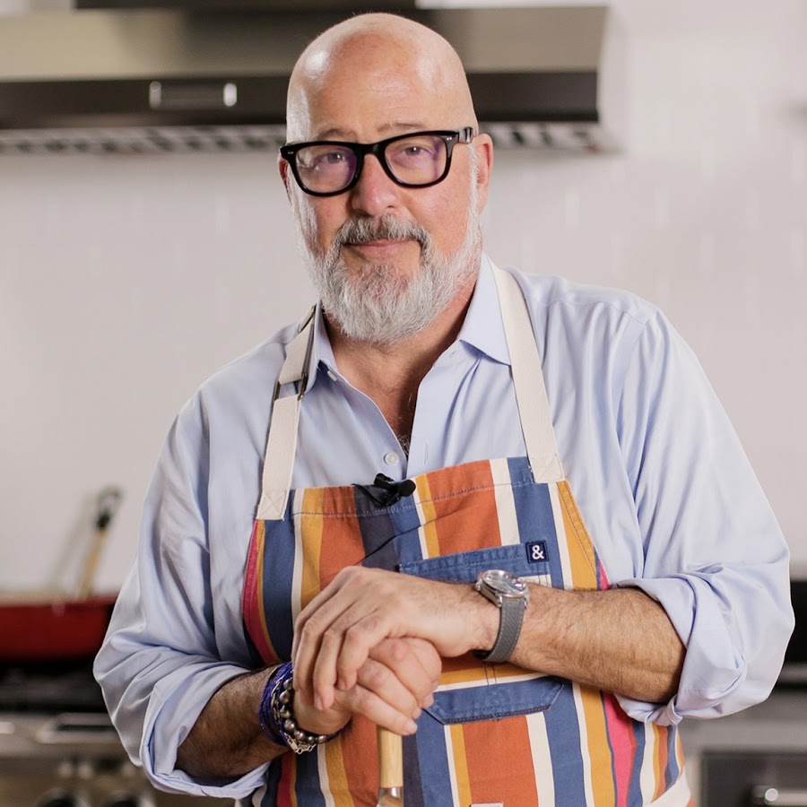 Bald man with glasses wearing a colorful striped apron in a kitchen.