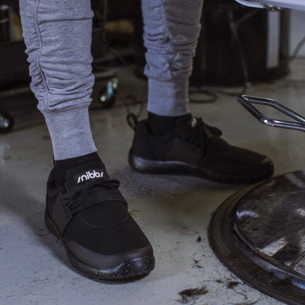 Person wearing black sneakers and gray pants standing on a floor with hair clippings.
