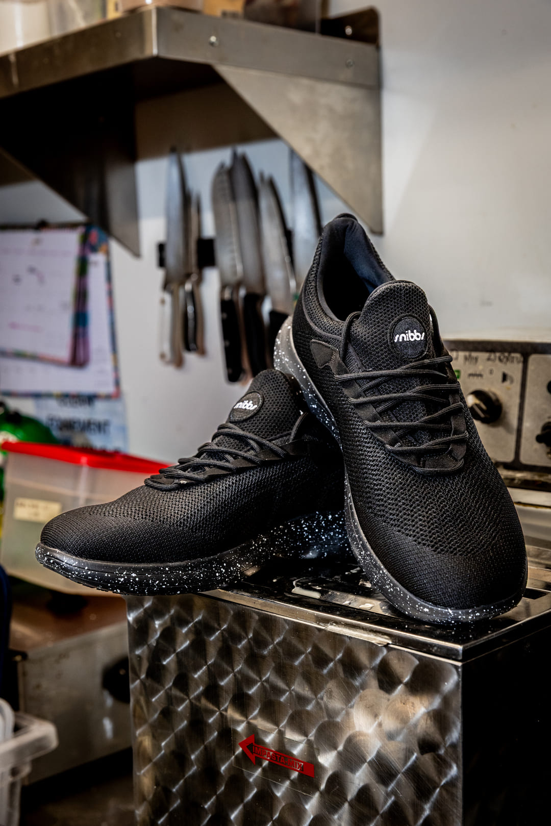 Black sneakers with speckled soles on a metal surface in a kitchen setting.