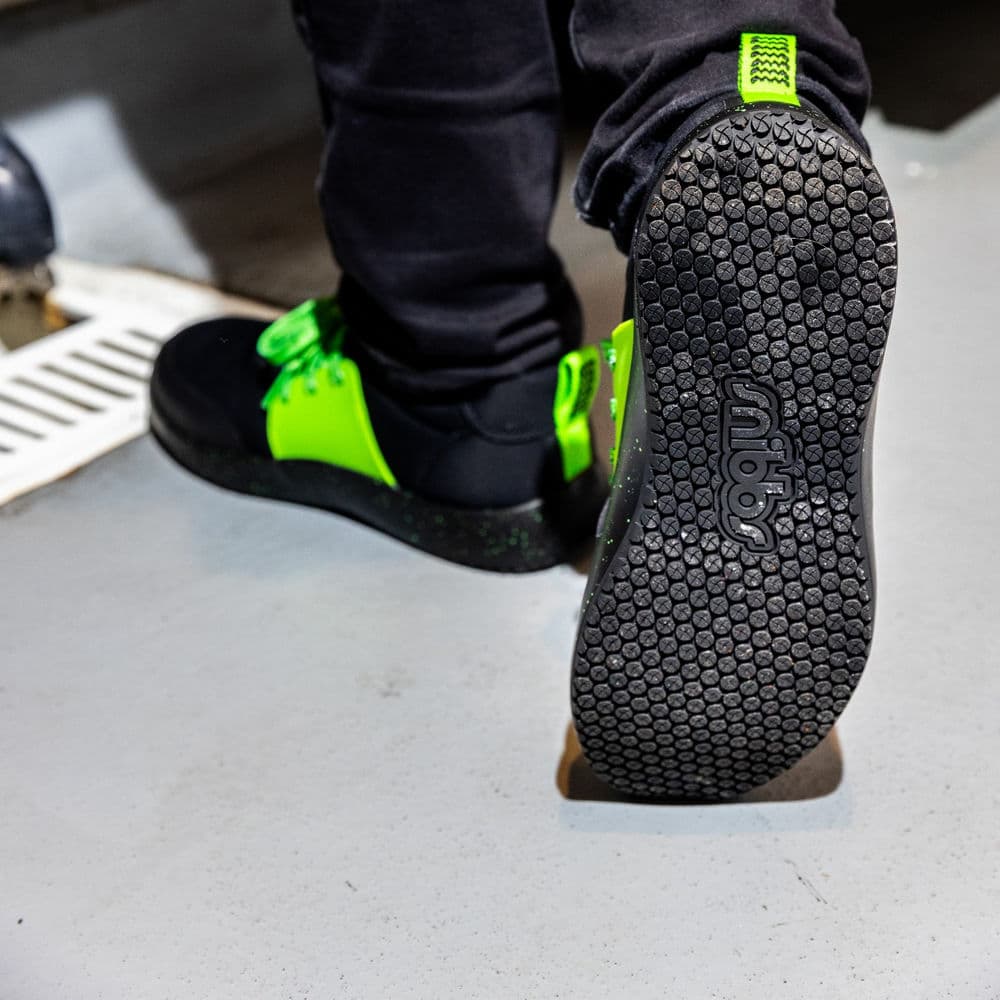 A close-up view of the sole of a black and neon green non-slip shoe.