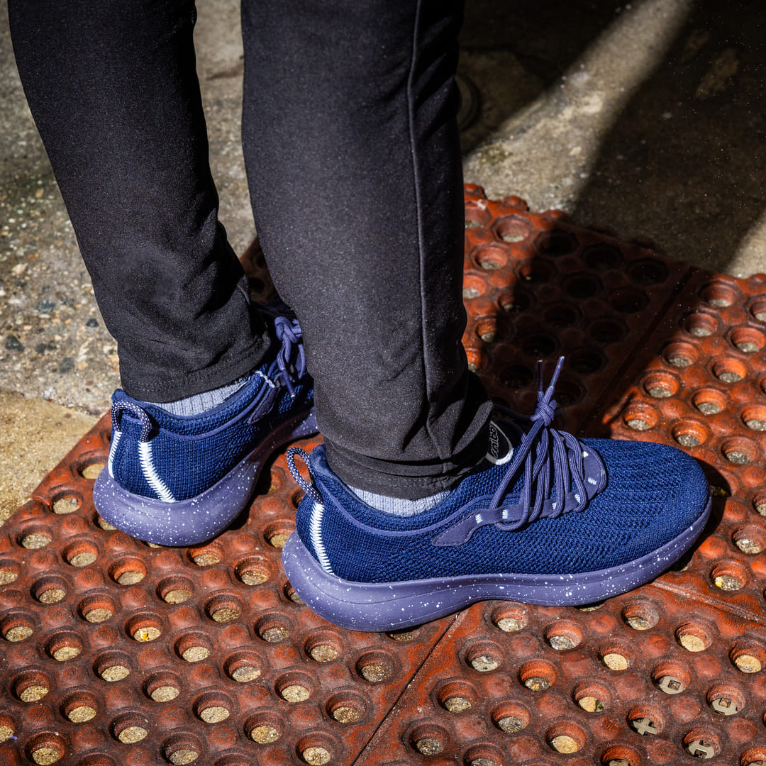 Person wearing black sneakers and gray pants standing on a floor with hair clippings.