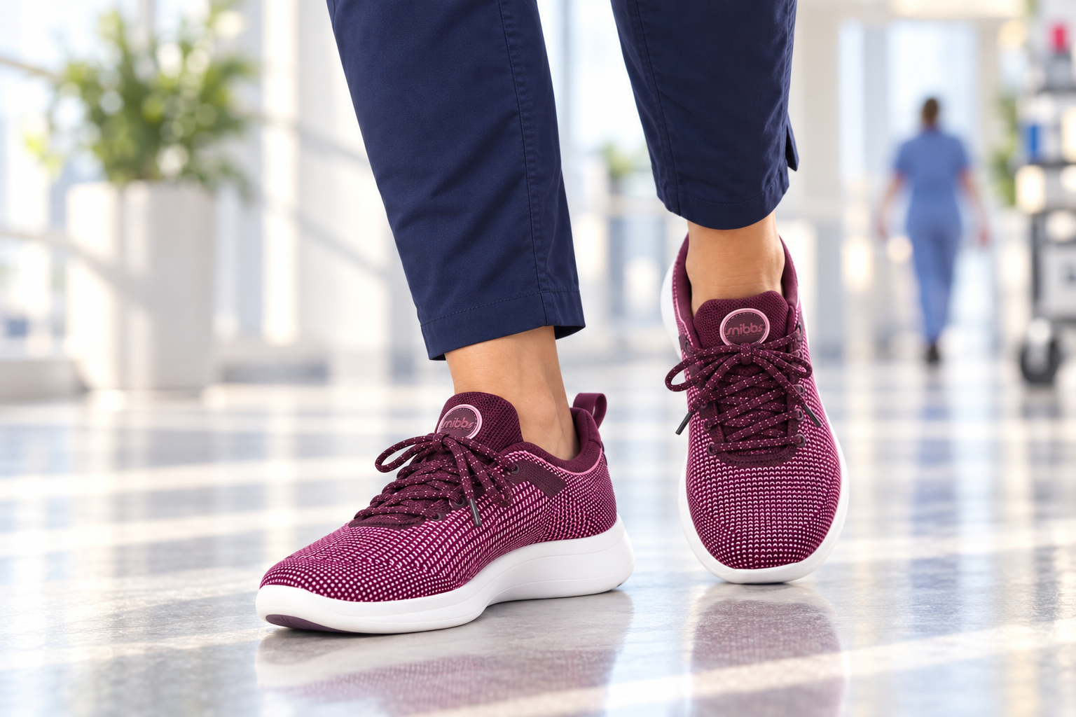 A close-up of a person wearing maroon sneakers and navy pants walking down a brightly lit hallway.