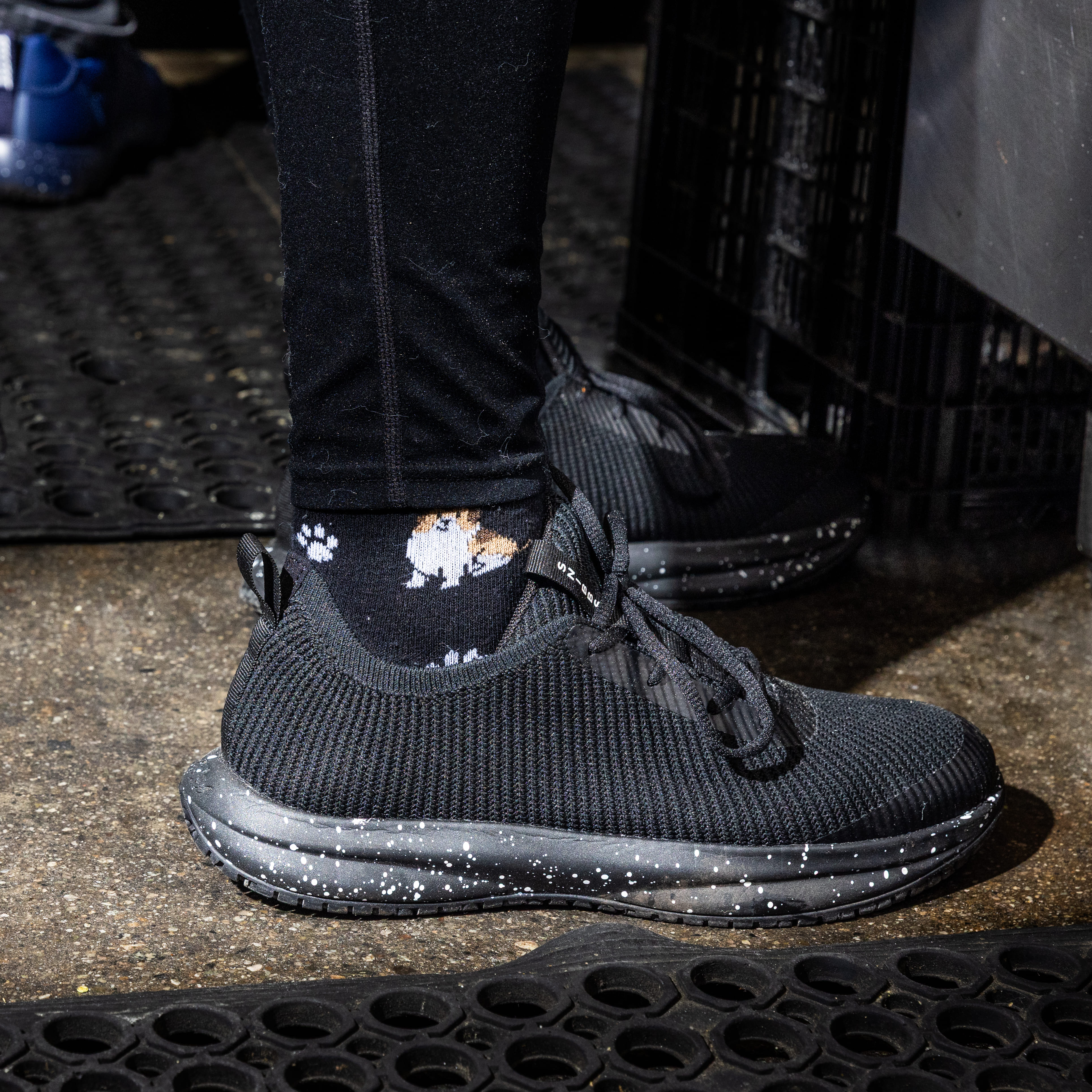 Person wearing black sneakers and cat-patterned socks on a textured floor.