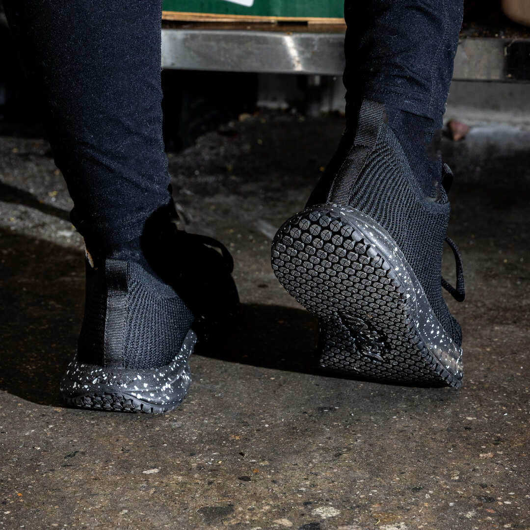 Person wearing black sneakers with speckled soles on a concrete floor.