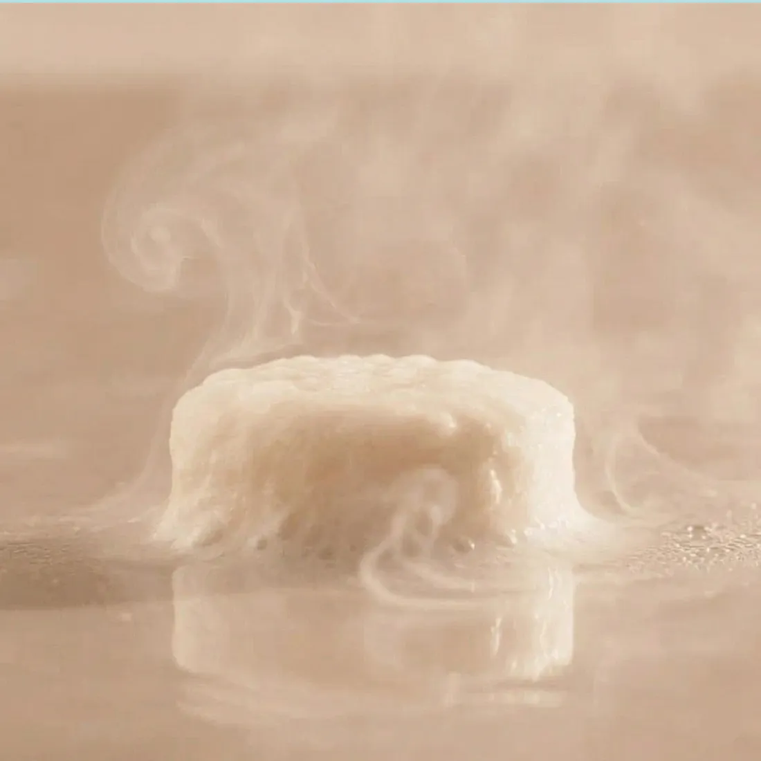 A close-up of a white, round object fizzing and releasing smoke-like vapor on a reflective surface.