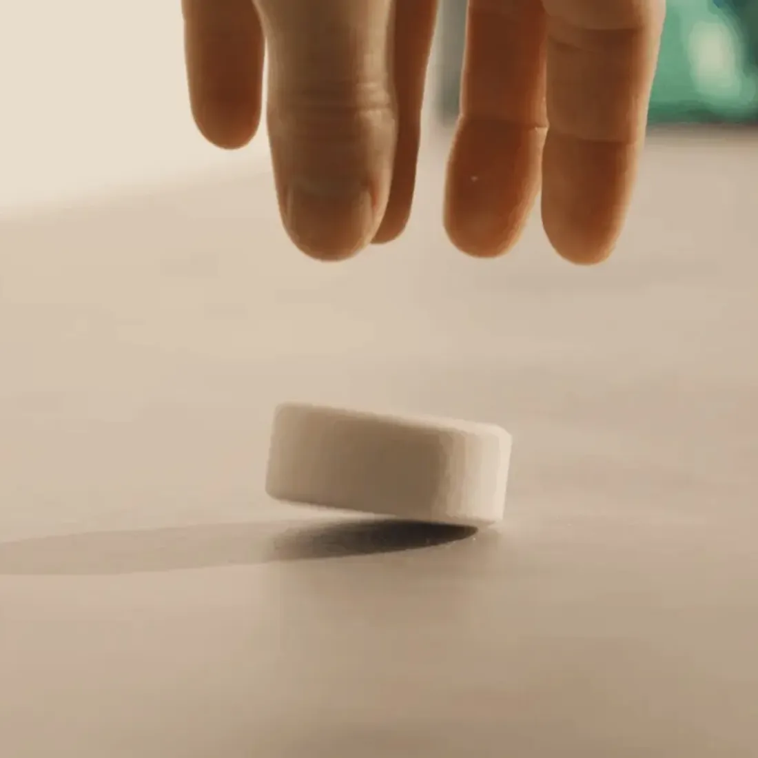 A close-up of a hand hovering over a small, white, circular object on a flat surface.