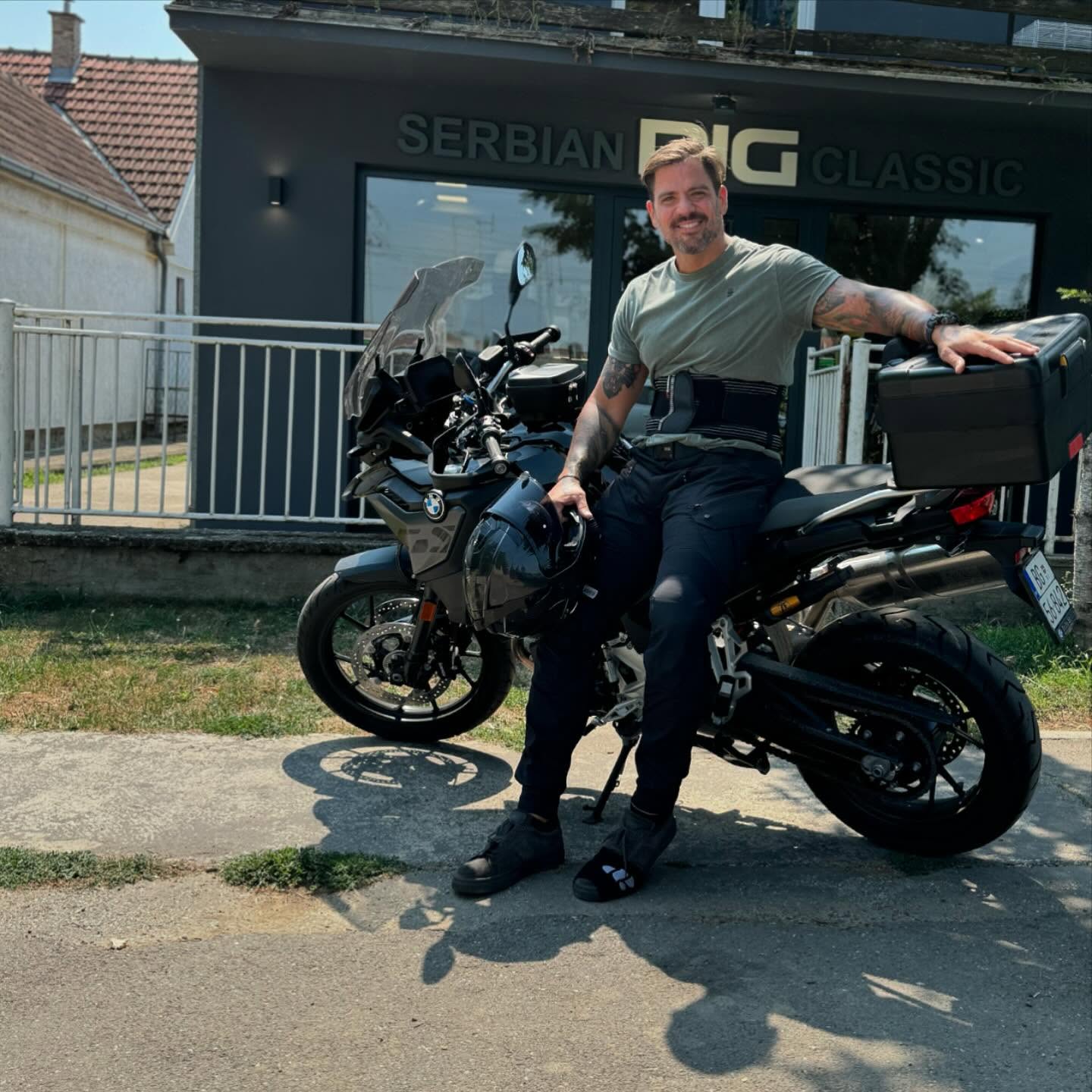 Person sitting on a motorcycle in front of a building with 'Serbian Big Classic' sign.