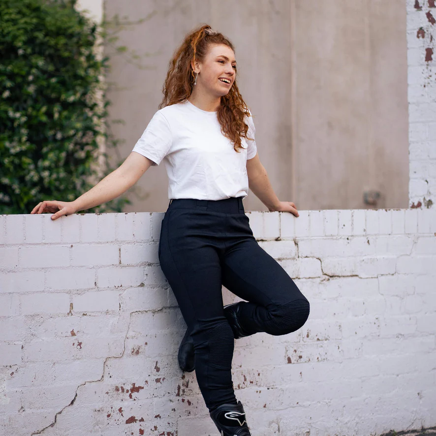 Person in white shirt and black pants leaning on a white brick wall.