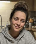 A woman with her hair in a messy bun, wearing a grey hoodie, smiles slightly at the camera.