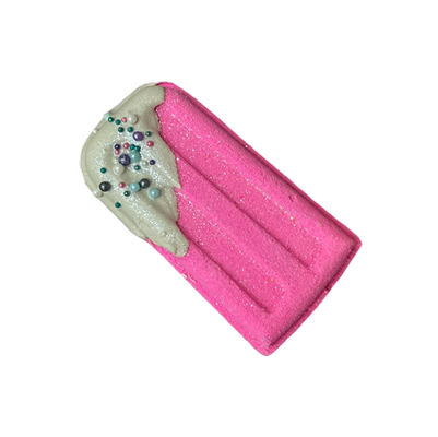 Pink popsicle-shaped bath bomb with white frosting and colorful sprinkles.