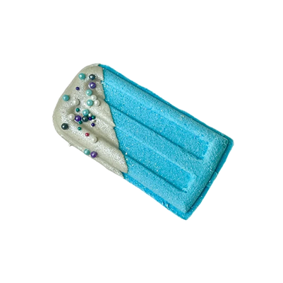 Blue popsicle-shaped bath bomb with white frosting and colorful sprinkles.