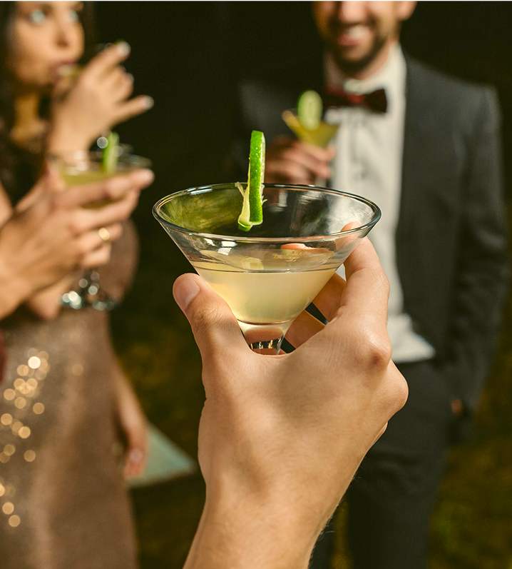 People holding cocktails with lime garnish at a social gathering.