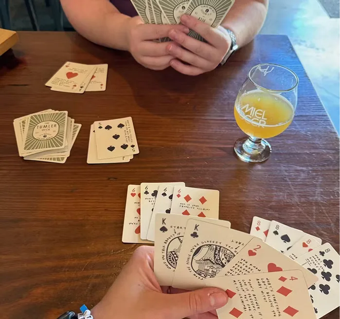 Two people playing cards at a table with a glass of beer.