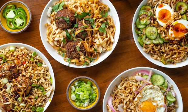 Five bowls of noodles with various toppings on a wooden table.