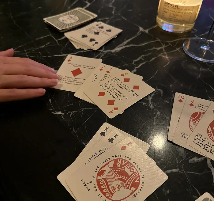 Playing cards spread out on a dark marble table with a hand reaching for them.