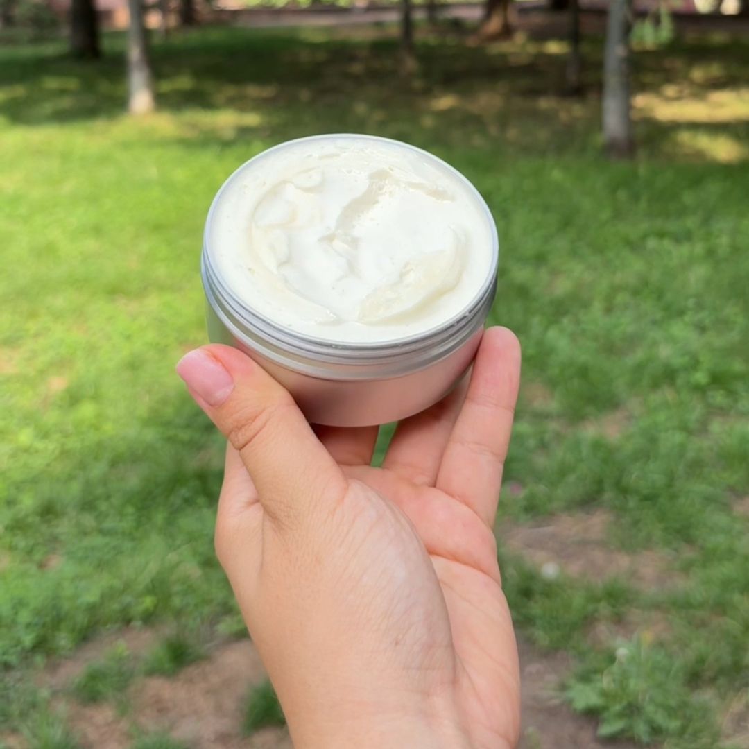 Hand holding a jar of cream outdoors on a grassy background.