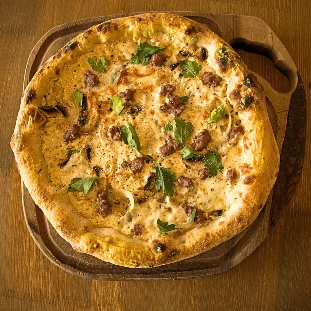 Pizza with sausage, mushrooms, and parsley on a wooden board.