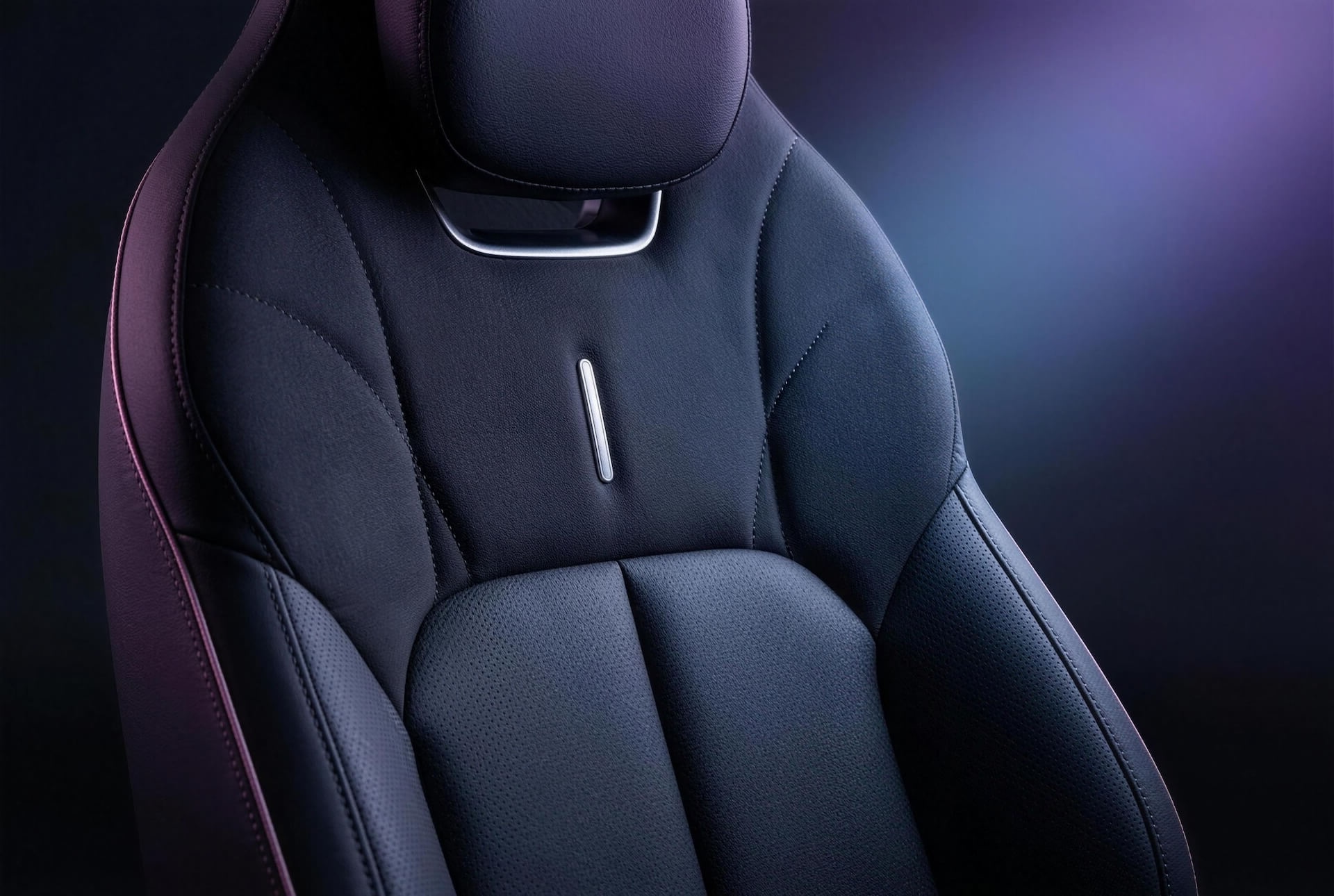 A close-up of a black leather car seat with silver accents, under purple and blue lighting.