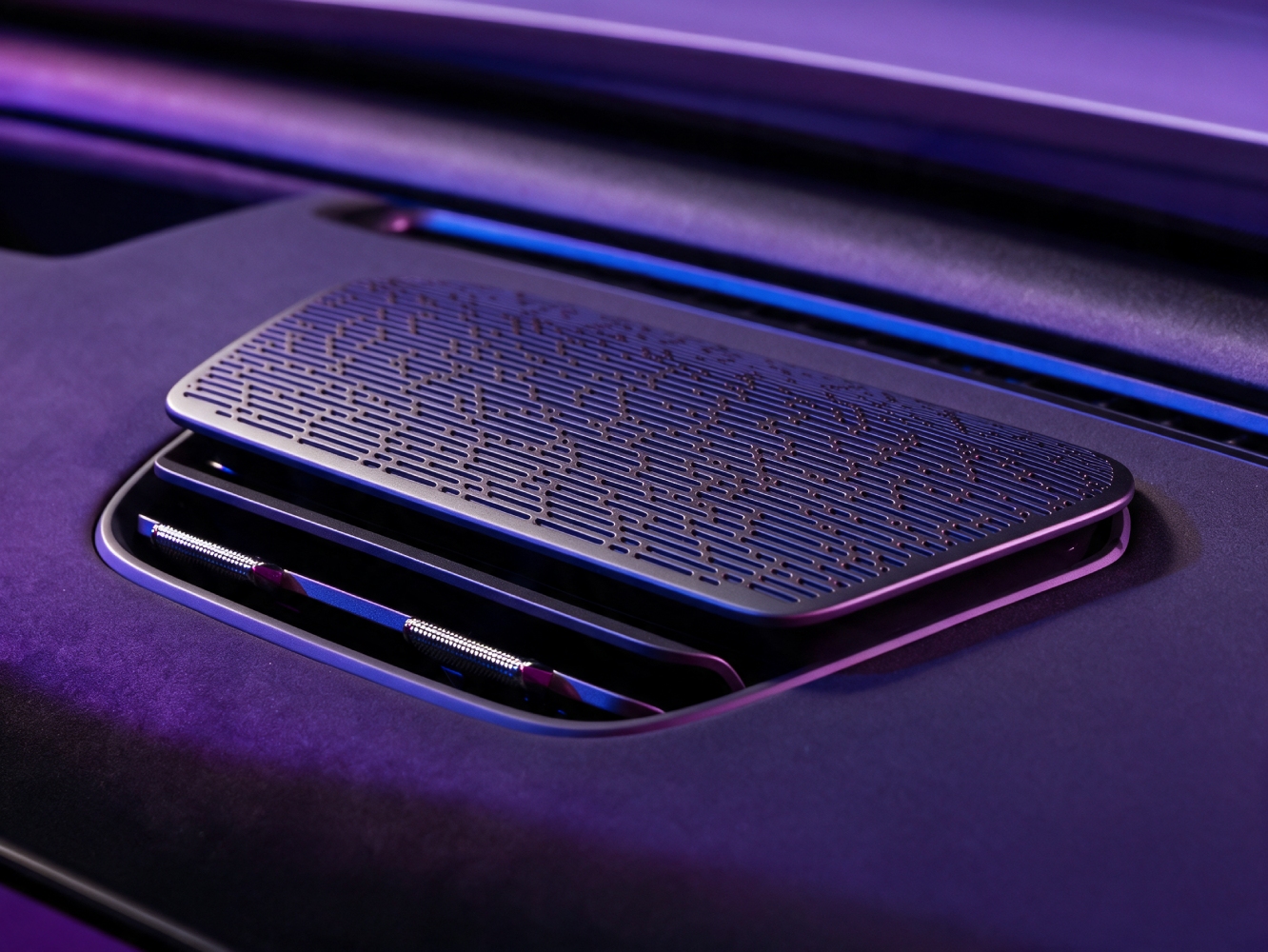 A close-up of a car's patterned dashboard air vent, illuminated by purple and blue light.