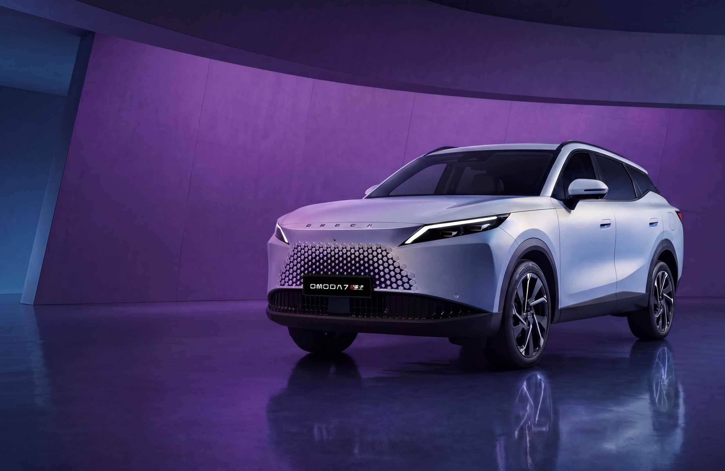 A white OMODA 7 SUV is parked in a studio with a purple-lit wall and a reflective floor.