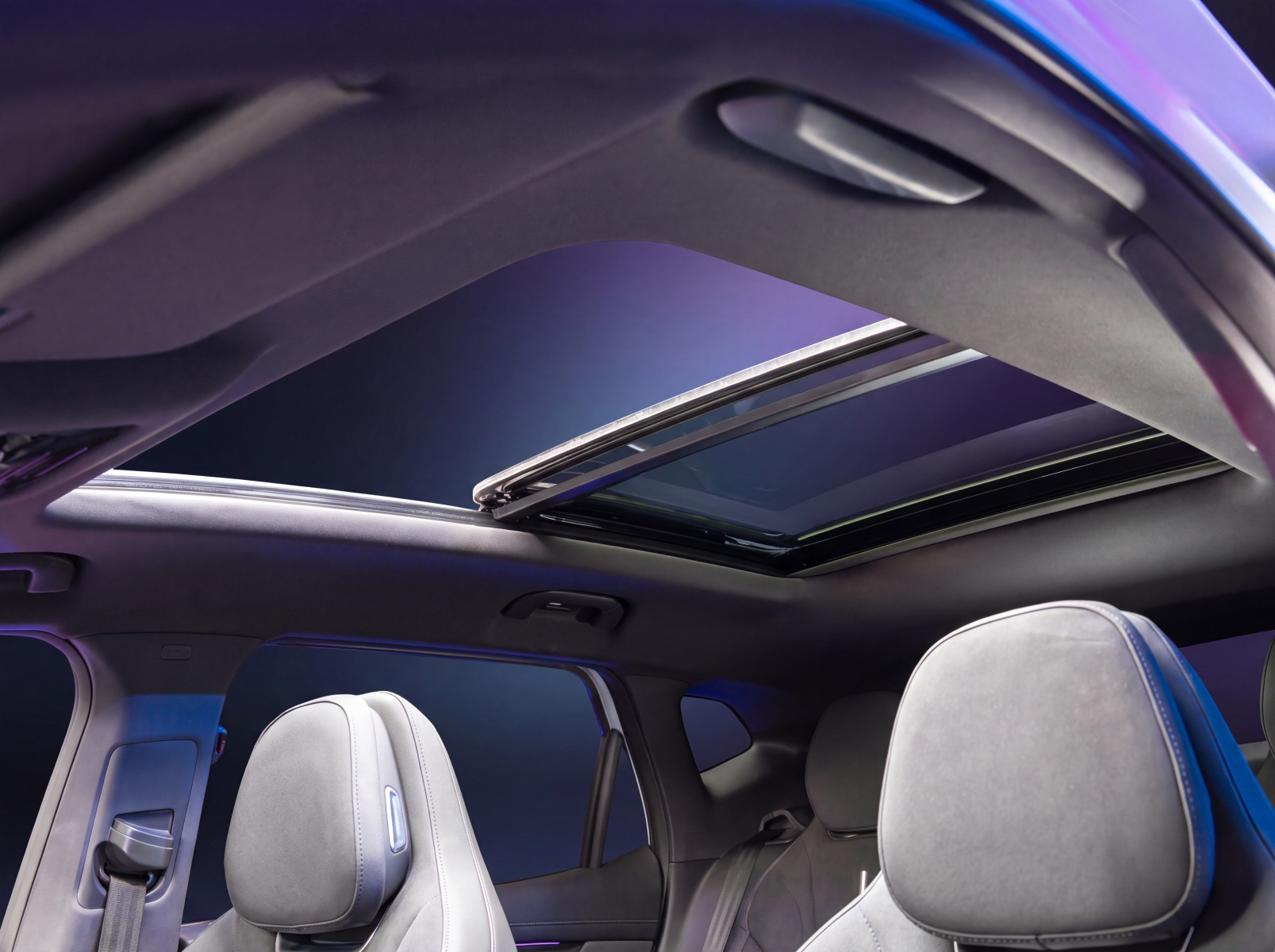 A view from inside a car looking up at an open panoramic sunroof and grey headrests.