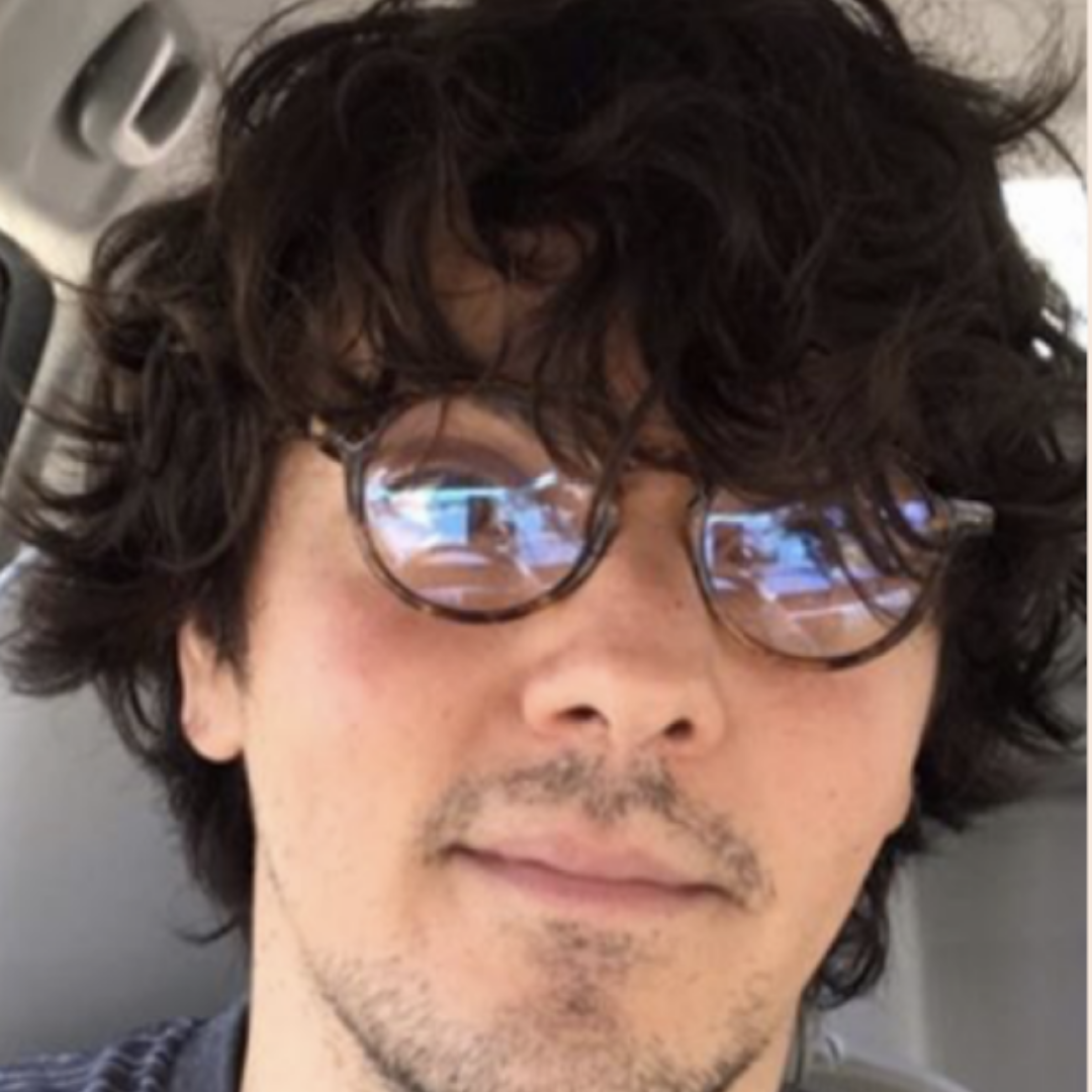 Person with curly hair and glasses sitting in a car.