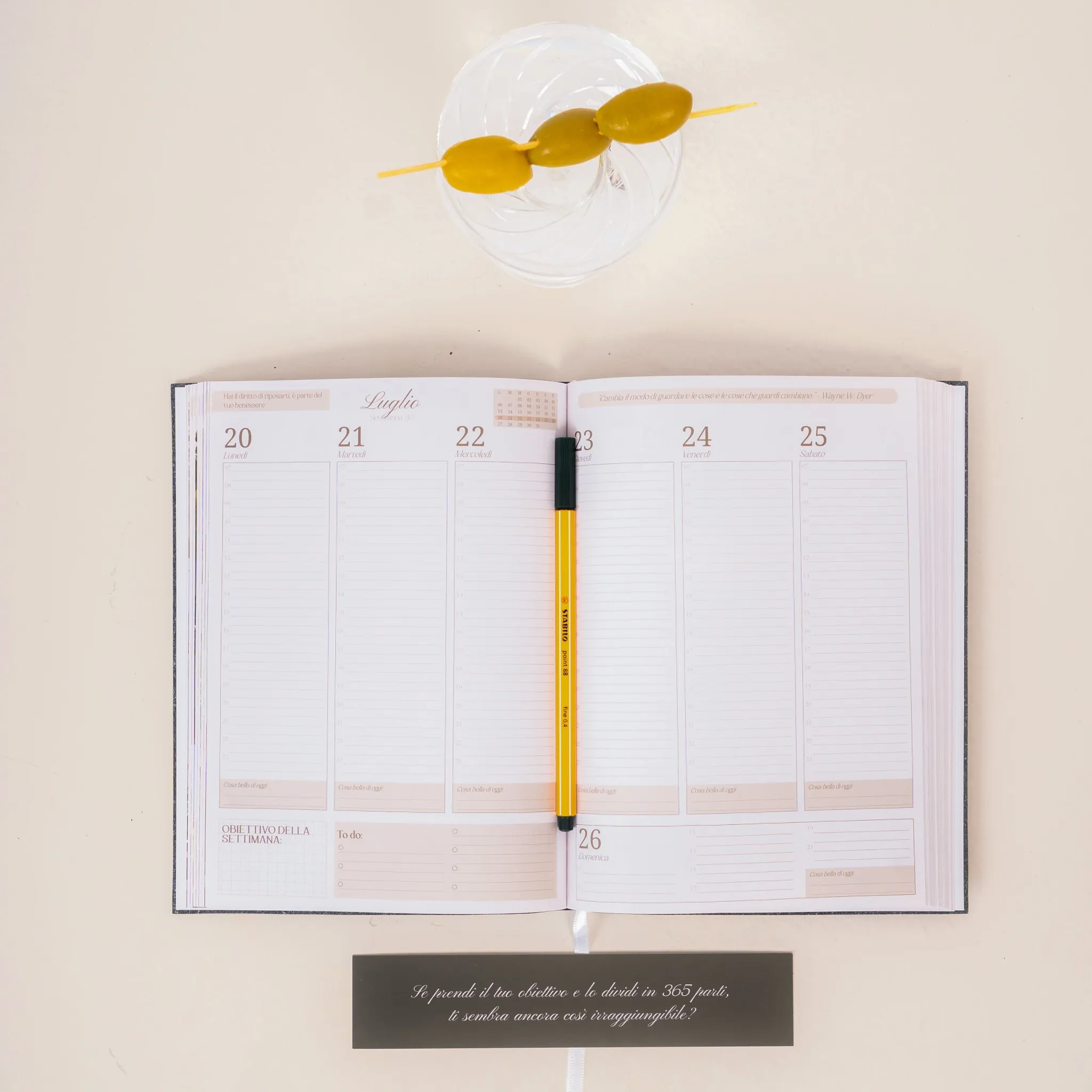 Open planner with a yellow pen and a glass with skewered olives.