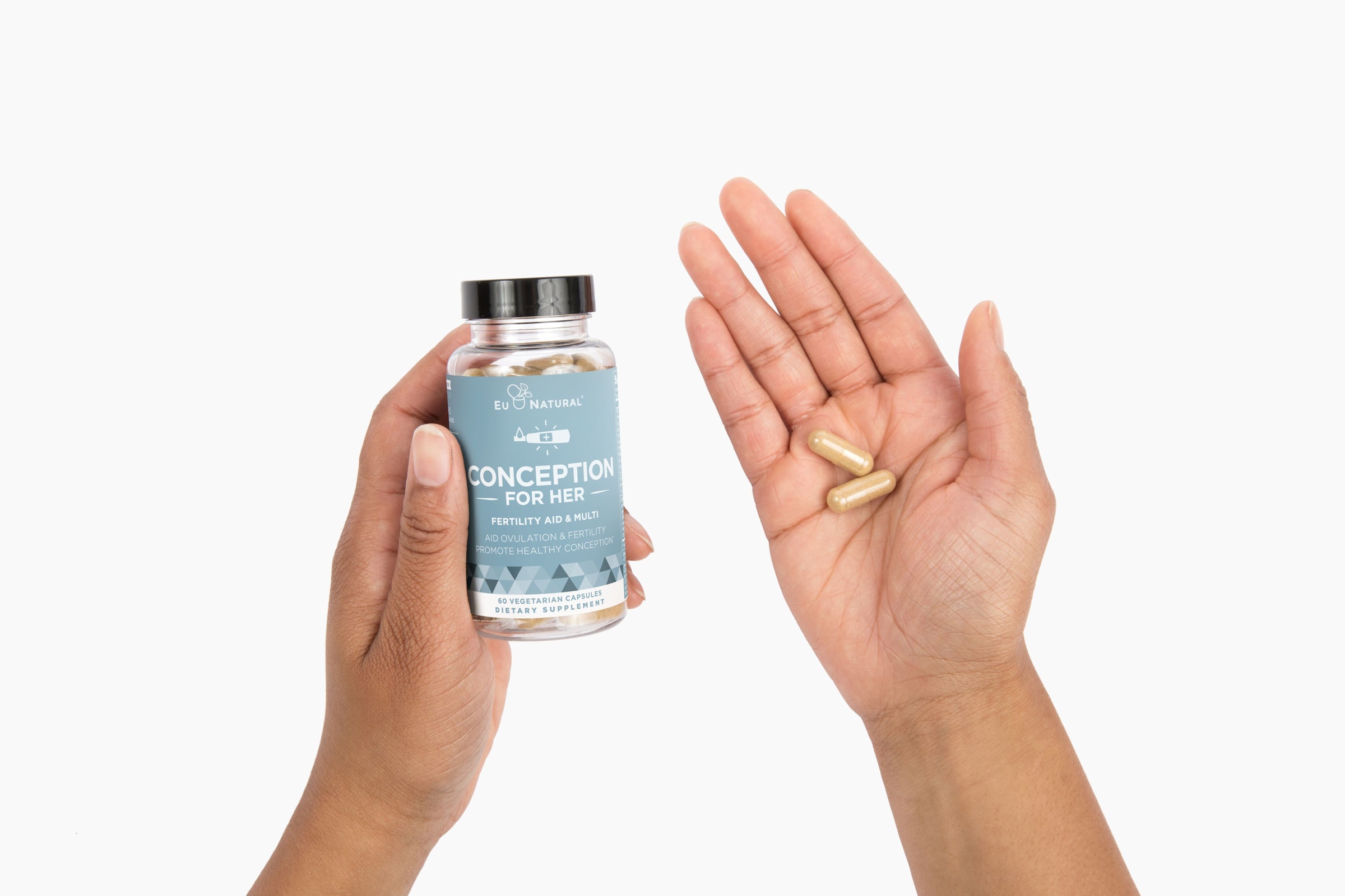 A person holds a bottle of EU Natural Conception for Her supplements and two capsules in their hands.