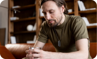 Man sitting on a couch holding a glass, looking pensive.
