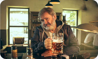 Older man sitting at pub, holding a large glass of beer.