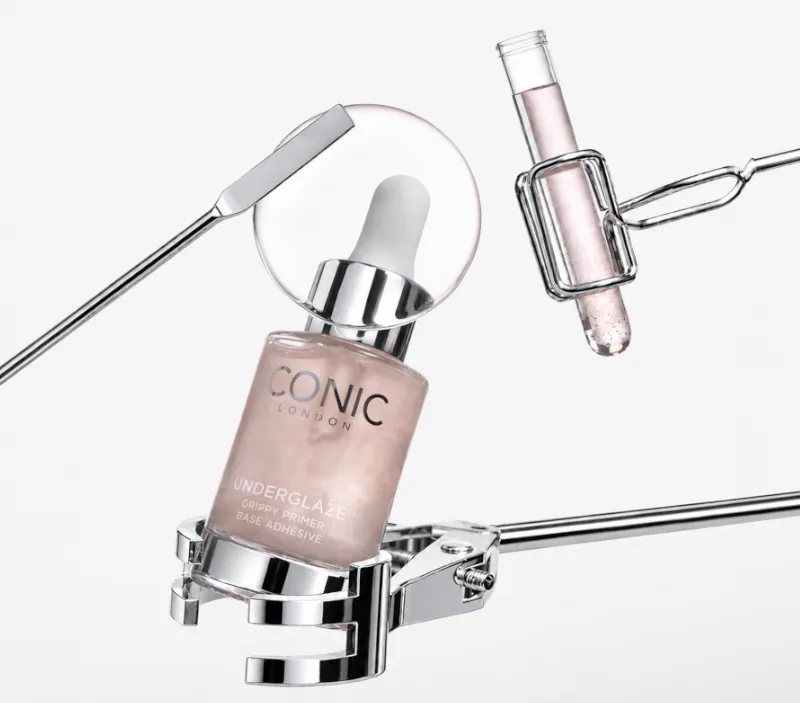 A bottle of Iconic London primer and a test tube held in scientific clamps against a white background.