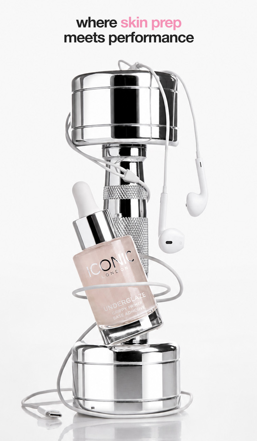 A bottle of Iconic London primer leans against a chrome dumbbell, with white earphones wrapped around them.