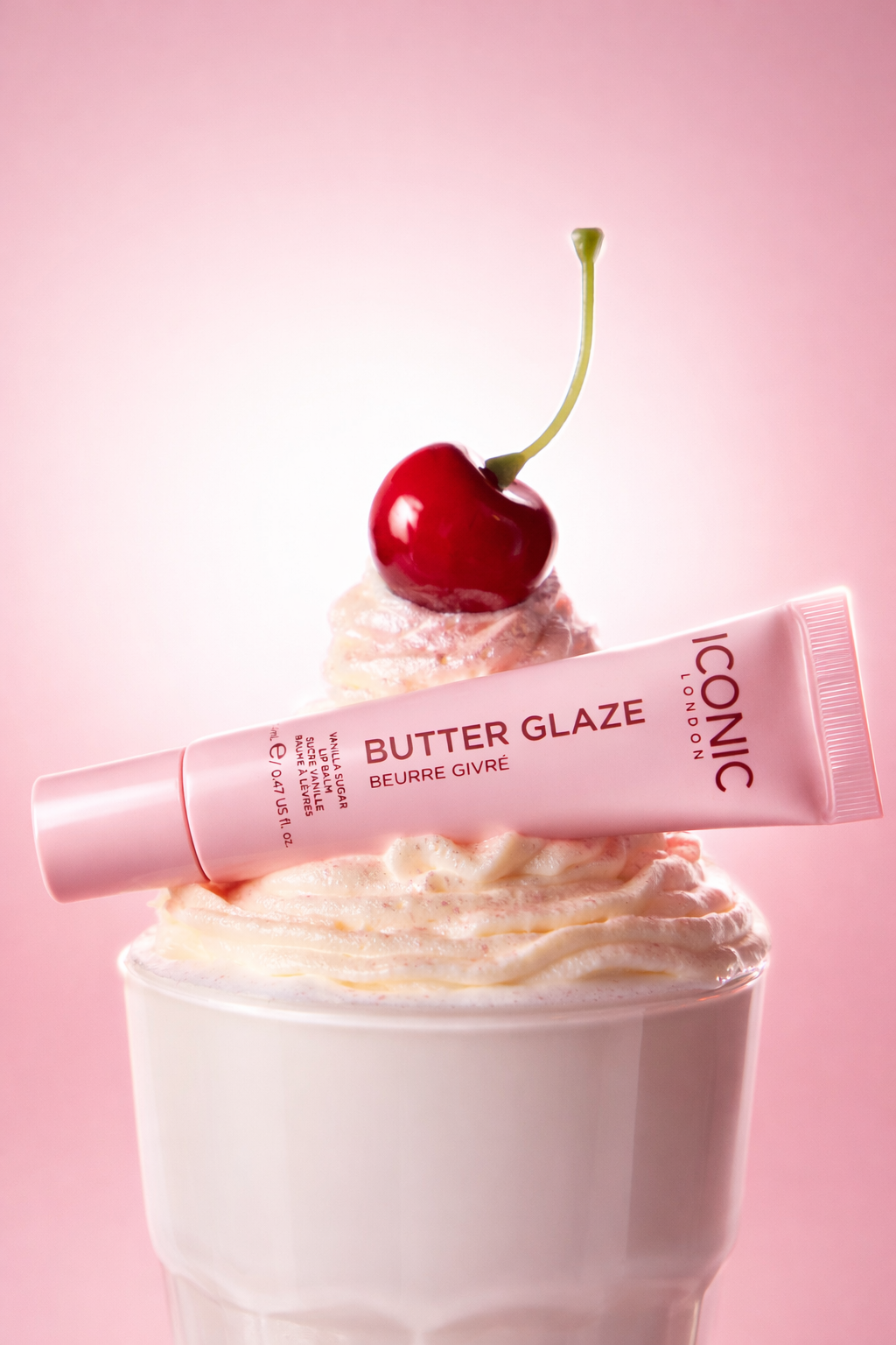 A pink tube of Iconic London lip balm rests on a swirl of whipped cream topped with a cherry.