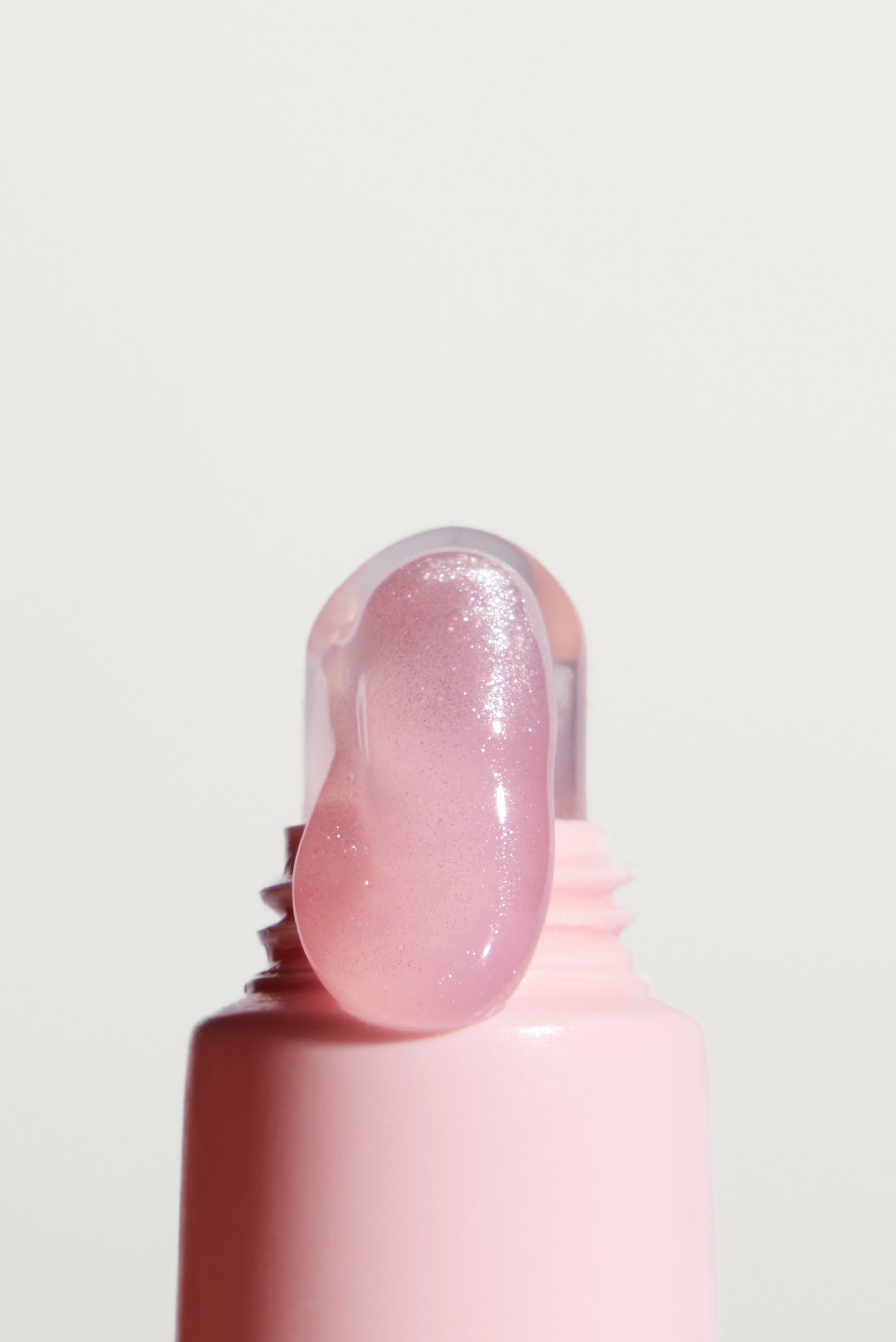 A close-up of a shimmery pink gel being squeezed from a pink tube onto a clear applicator.